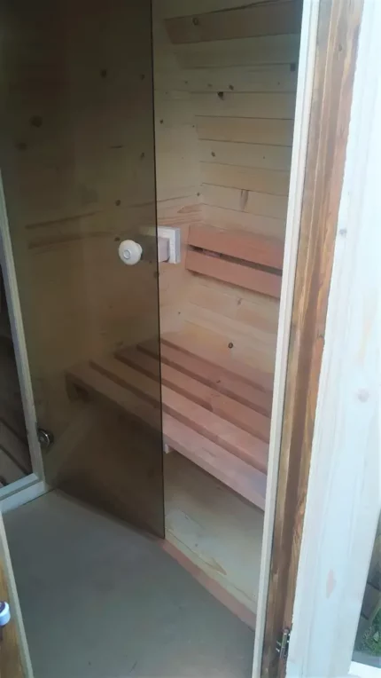 Przedsionek sauny ogrodowej z otwartymi drzwiami oraz ławką